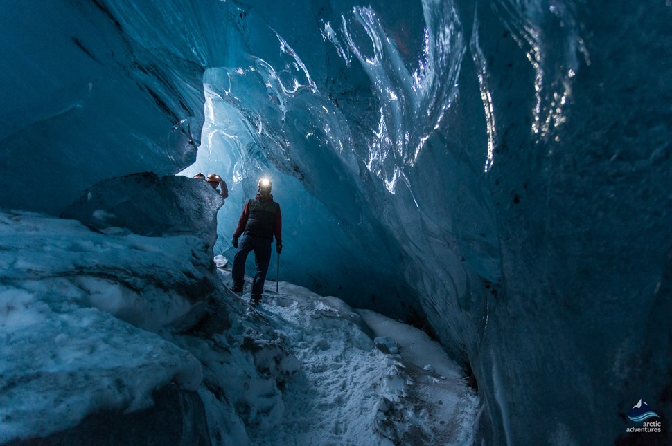 Person exploring inside an ice cave with walking sticks and a headlamp