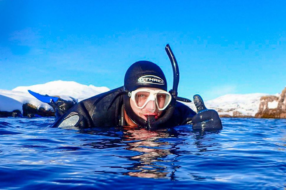 Close up of man in snorkelling suit and goggles in deep blue sea at Silfra Fissure in Iceland, showing a thumbs up.