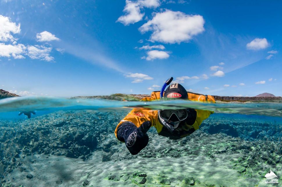 Man  in orange suit with googles snorkeling in crystal clear sea, showing thumbs up.