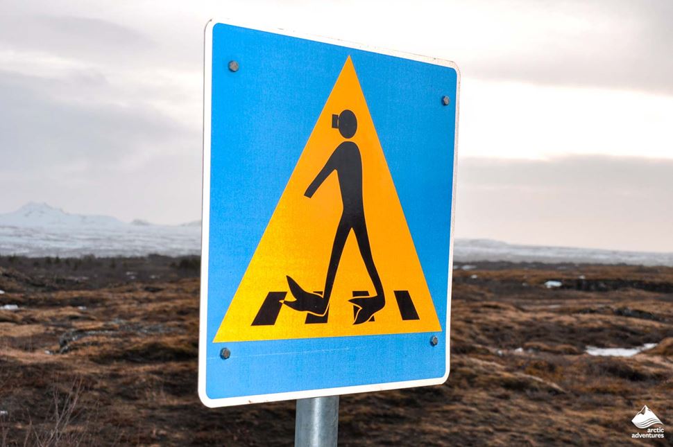 Yellow and blue sign of a person with snorkeling gear at zebra crossing in Silfra Fissure, Iceland.