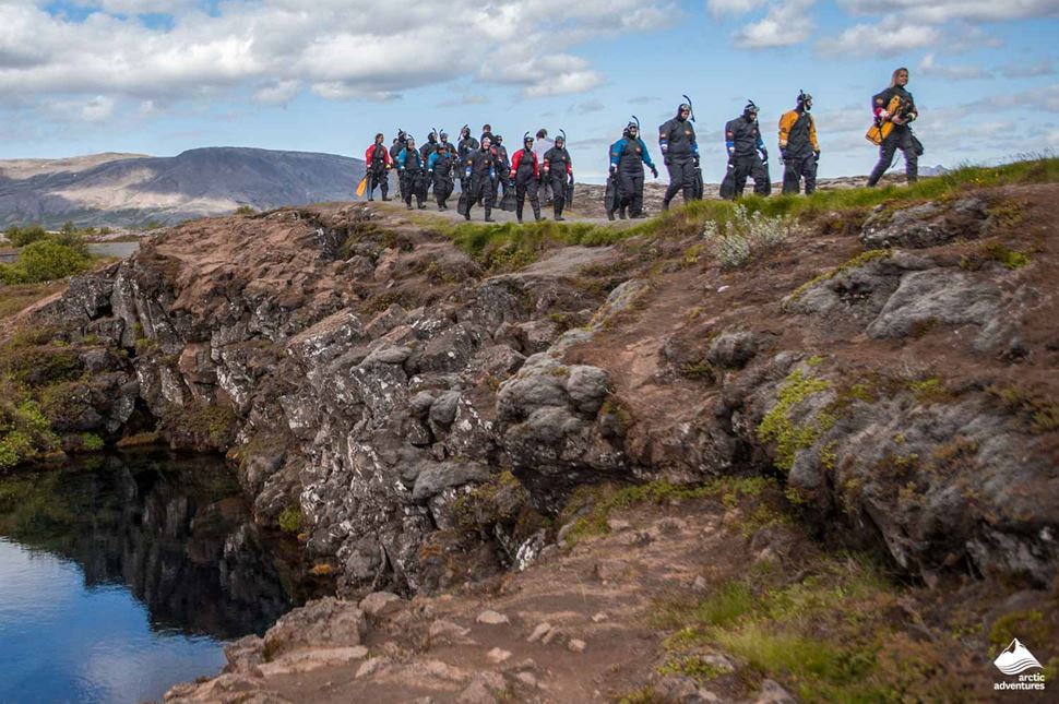 Group of people walking by rocky Silfra Fissure lake getting ready to go snorkeling.