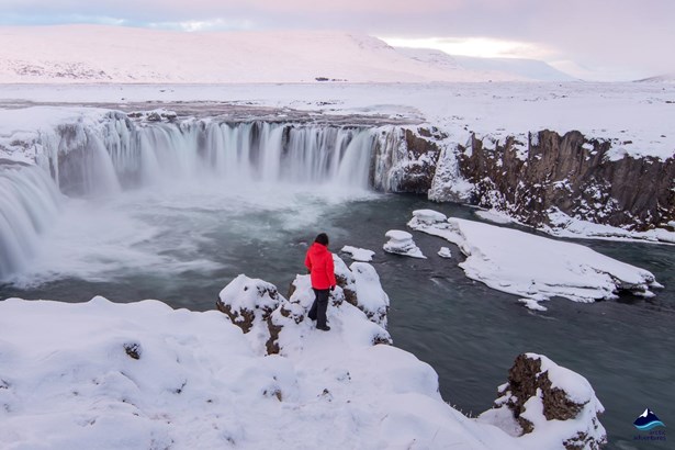 woman with red jacket standing near Godafoss waterfall