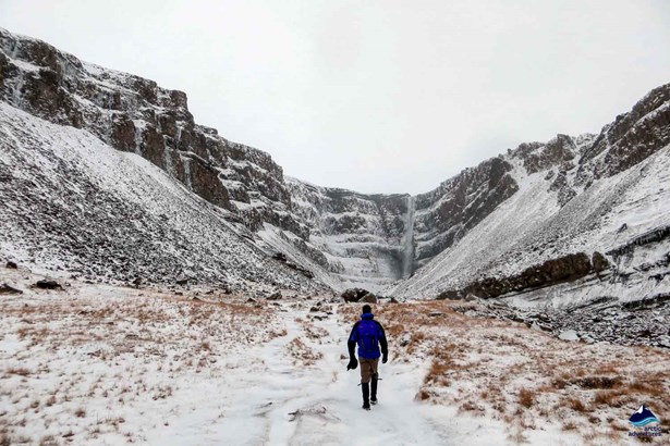 man walking to Hengifoss Waterfall by snowy road
