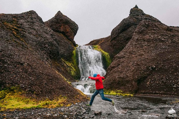 man crossing river near waterfall in Iceland
