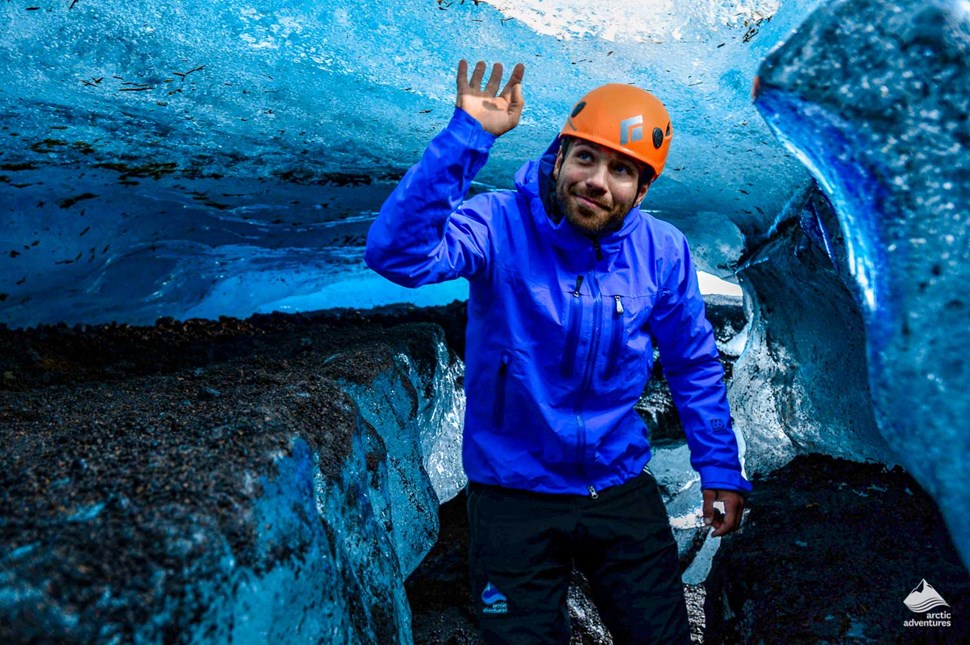 A man in a helmet walking underneath a sheet of ice in an ice cave