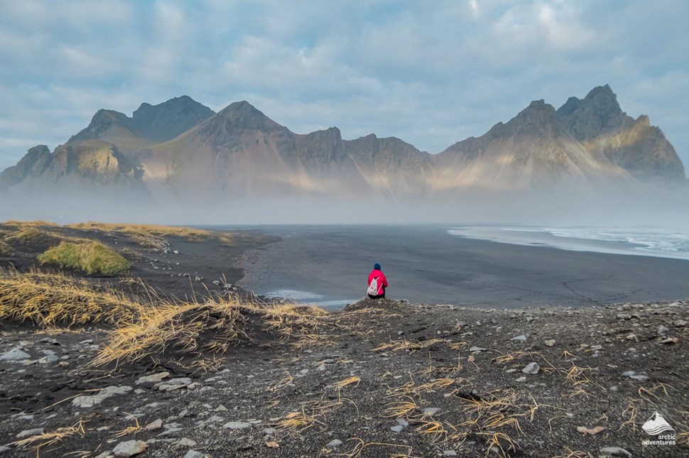 Human sitting on the edge with a view to Vestrahorn Mountain