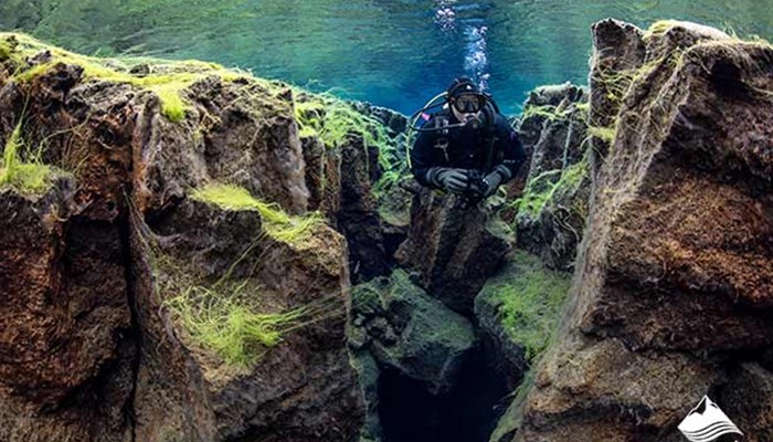 man Scuba Diving by the rocks in Silfra
