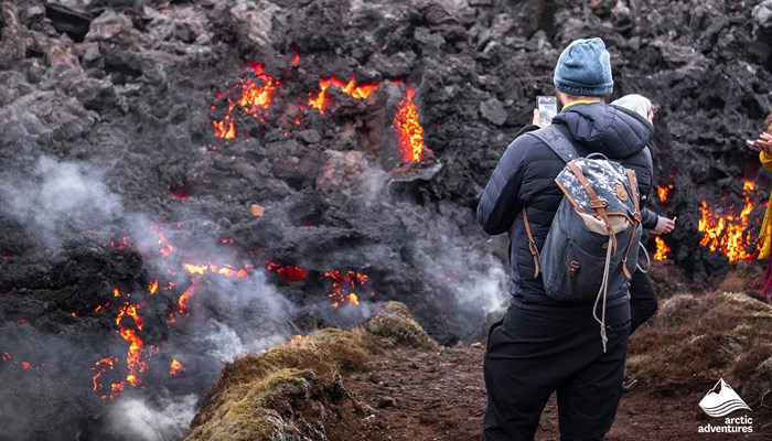 man taking pictures of hot volcano magma