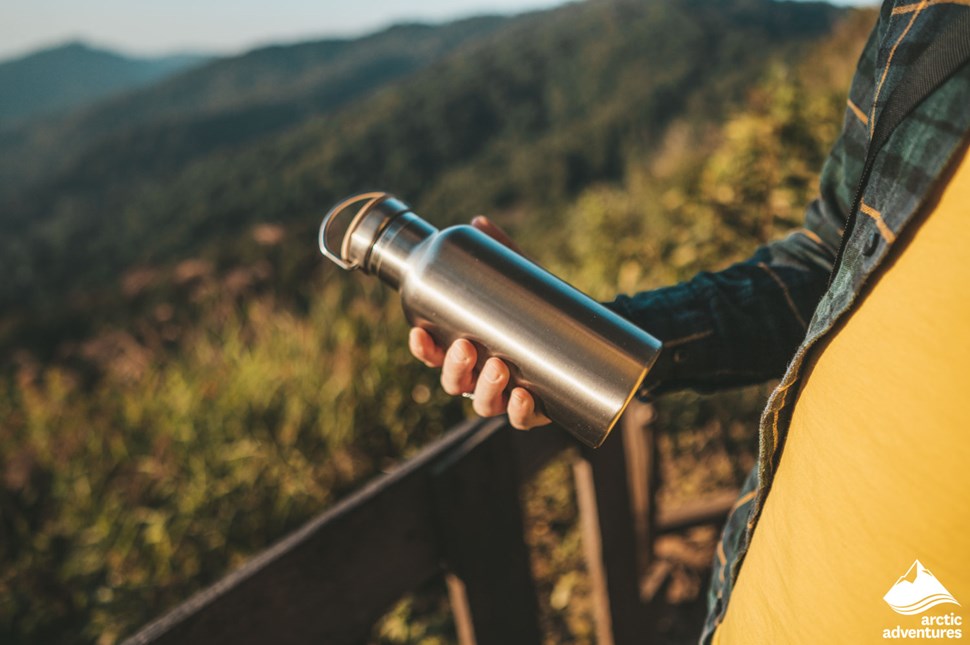 man holding thermos bottle in mountains