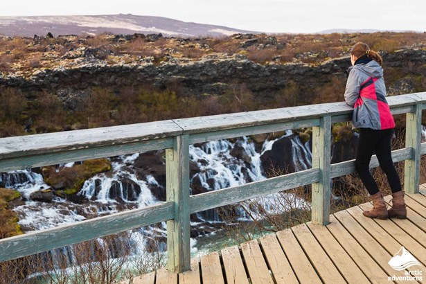 Woman Looking at Hraunfossar Waterfall from Bridge