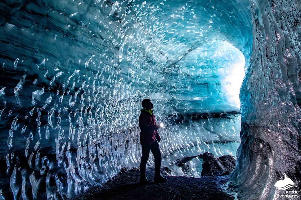 Man holding a flashlight and exploring a dark blue and bright blue ice cave in Iceland