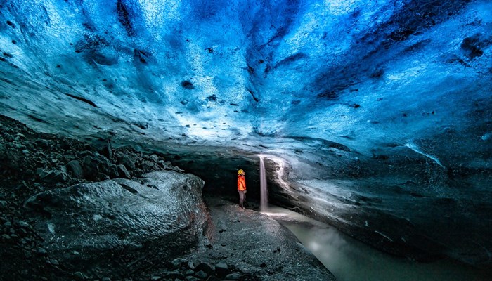 Interior view of a person exploring a dark blue ice cave in Iceland