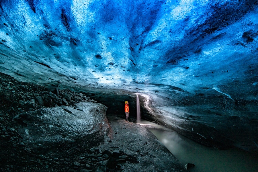 Interior view of a person exploring a dark blue ice cave in Iceland