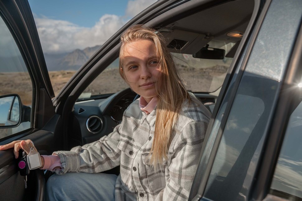Woman In Her Car With Icelandic Mountain Landscape On The Background