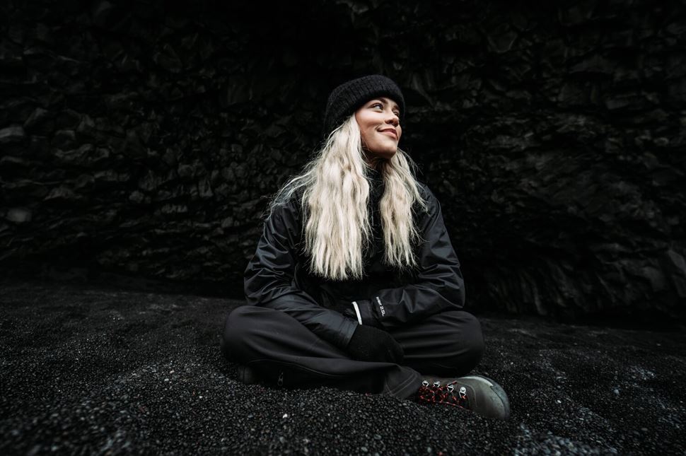 Woman wearing black coat and hat sitting on the beach Iceland