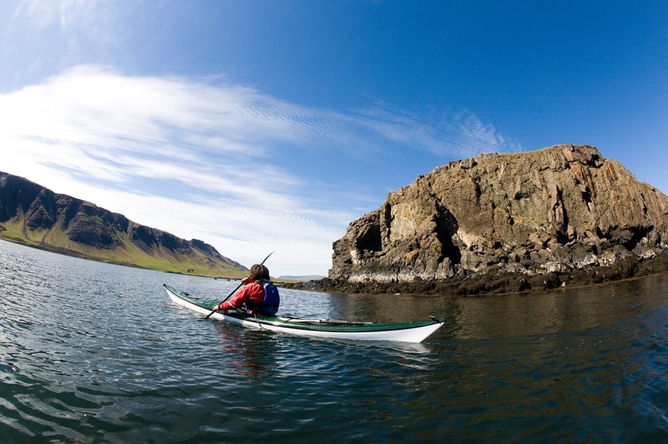 Kayaker on calm waters near rugged cliffs under a vast blue sky