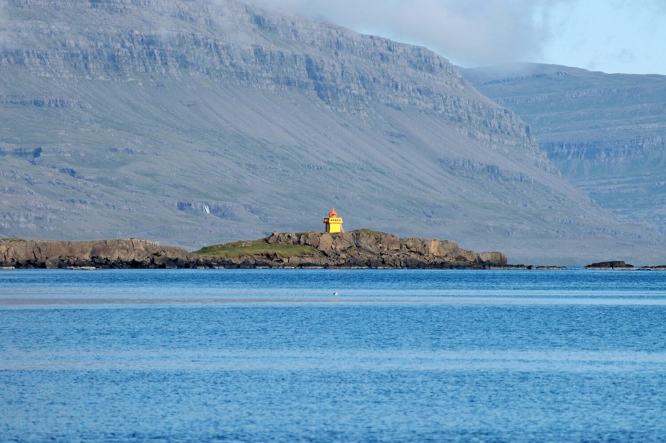 Yellow lighthouse perched on rocky outcrop against backdrop of rugged mountains and calm blue waters