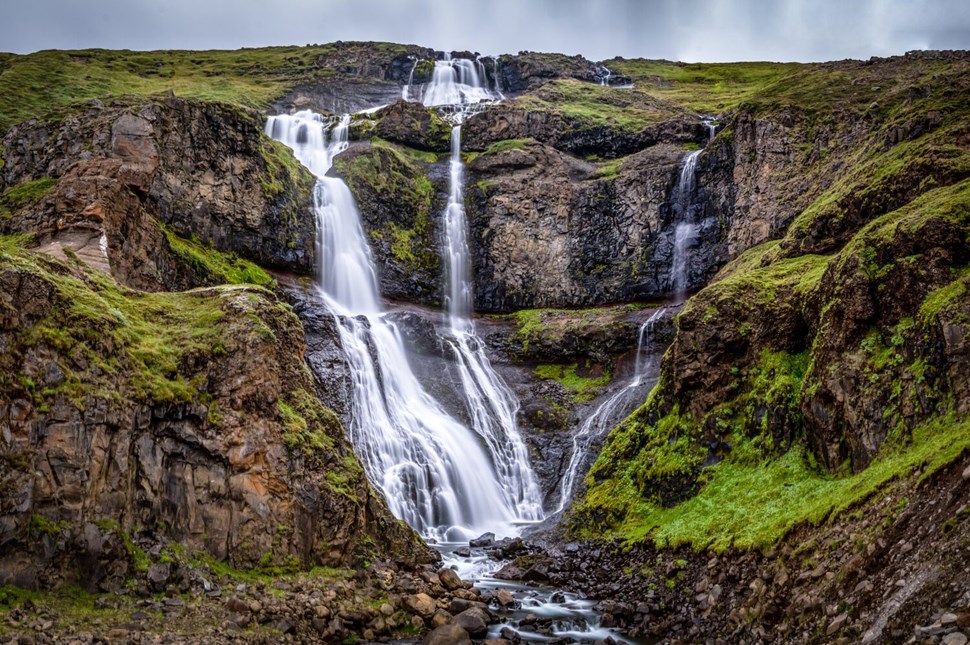 Cascading waterfalls flowing over moss-covered rocks in rugged landscape