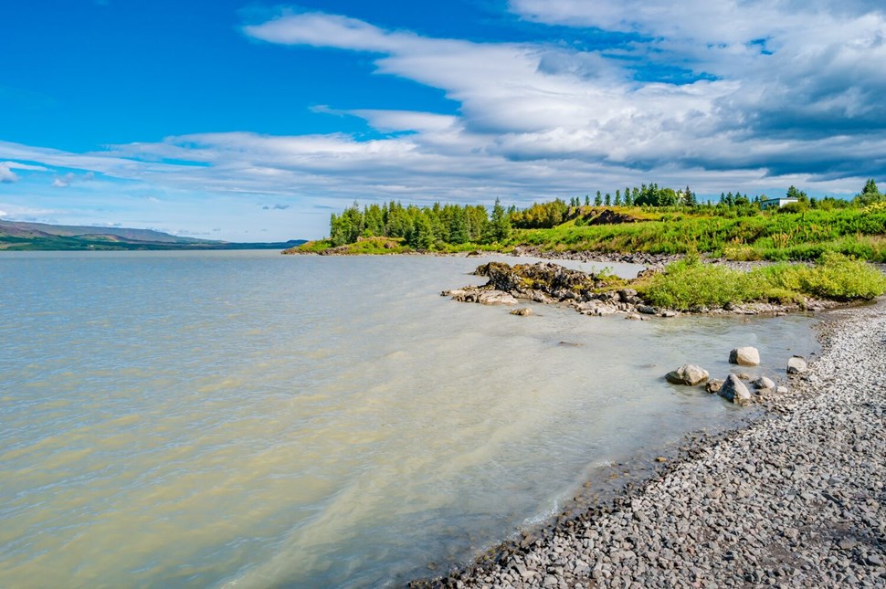 Picturesque lakeside view with clear waters, pebbled shoreline, and green landscape