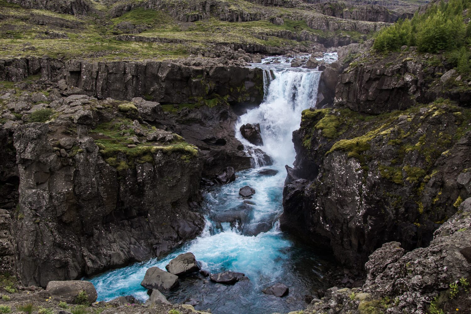 Rushing waterfall cascading through moss covered rocky cliffs amidst rugged terrain