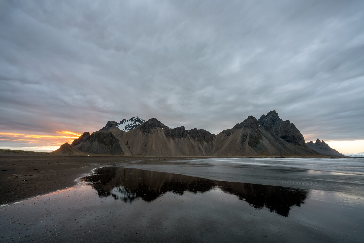 Dramatic mountain range reflecting on serene beach under moody sunset sky