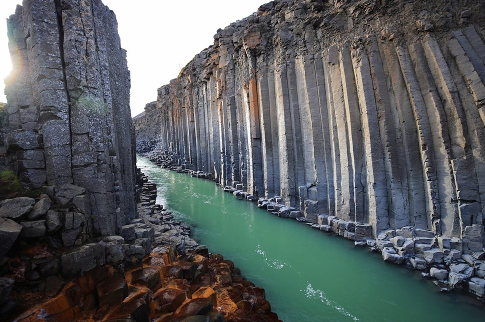 Towering basalt columns flank a turquoise river with sunlit rocky shores