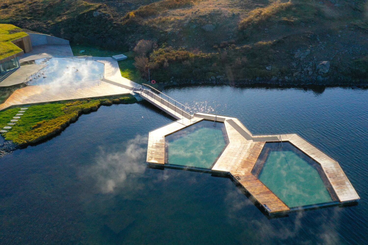Aerial view of geothermal pools in calm lake surrounded by grassy terrain
