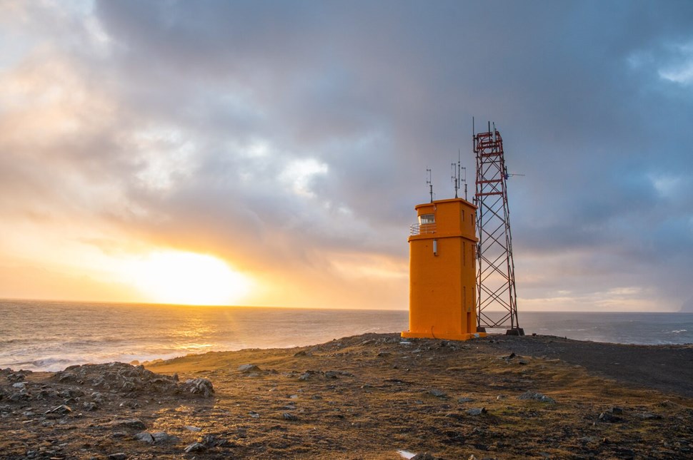  Golden sunset over the ocean with orange lighthouse and adjacent radio tower on rugged coastline