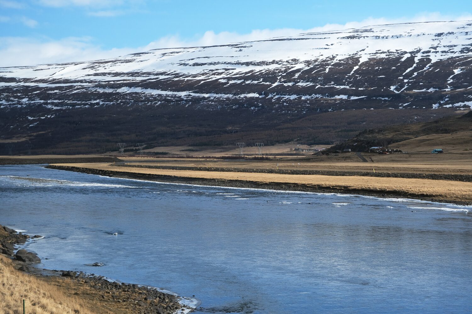 Snow capped mountains overlooking a serene river with distant settlements