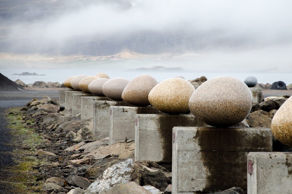 Row of polished stone eggs on concrete pedestals overlooking misty coastal landscape
