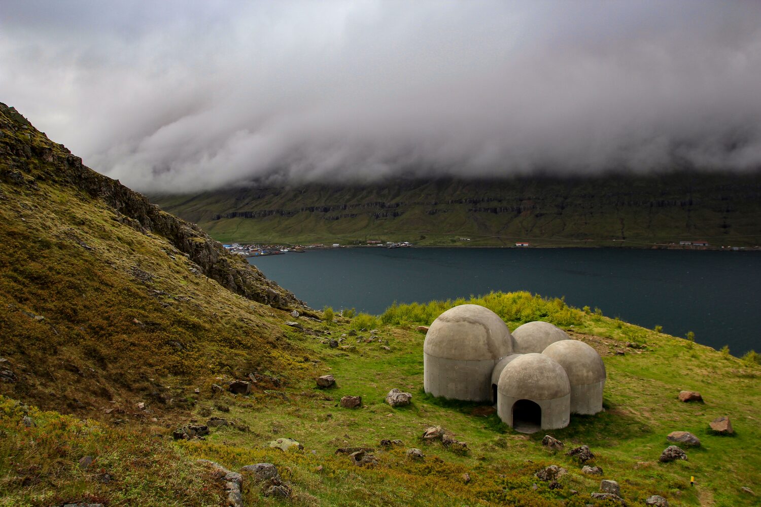 Dome shaped structures on green hillside overlooking a bay with distant mountains