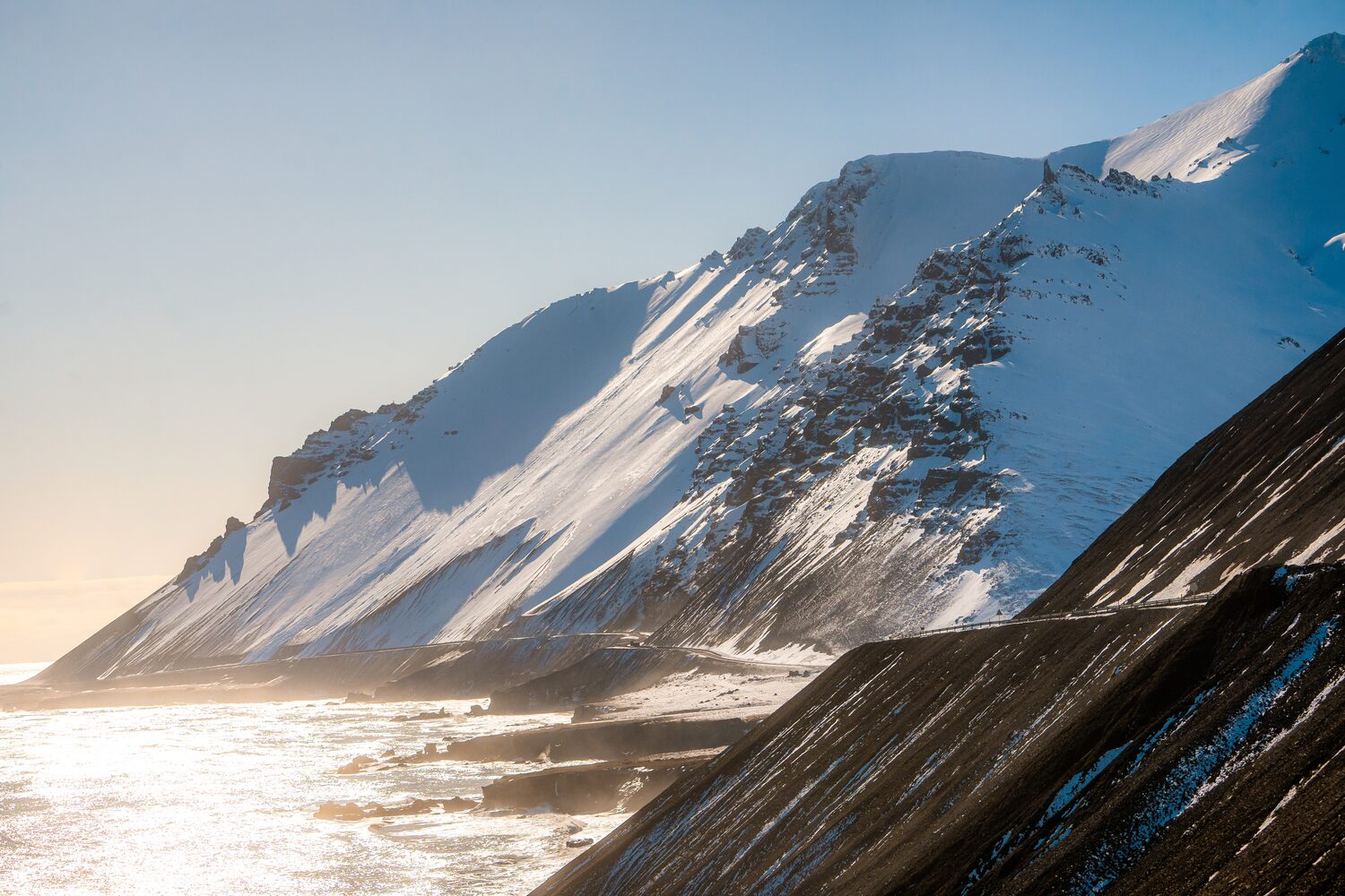 Snow covered mountain peaks reflecting sunlight beside shimmering icy coastline