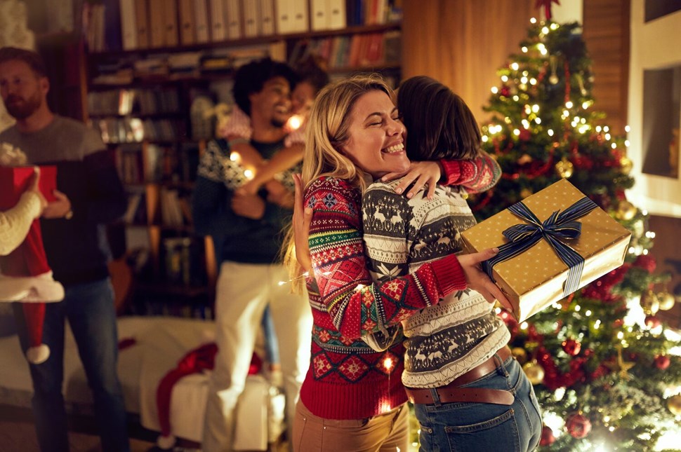 Joyful embrace during Christmas gift exchange by the festive tree.