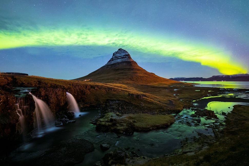 Northern Lights dance above Kirkjufell mountain and waterfalls in Iceland.