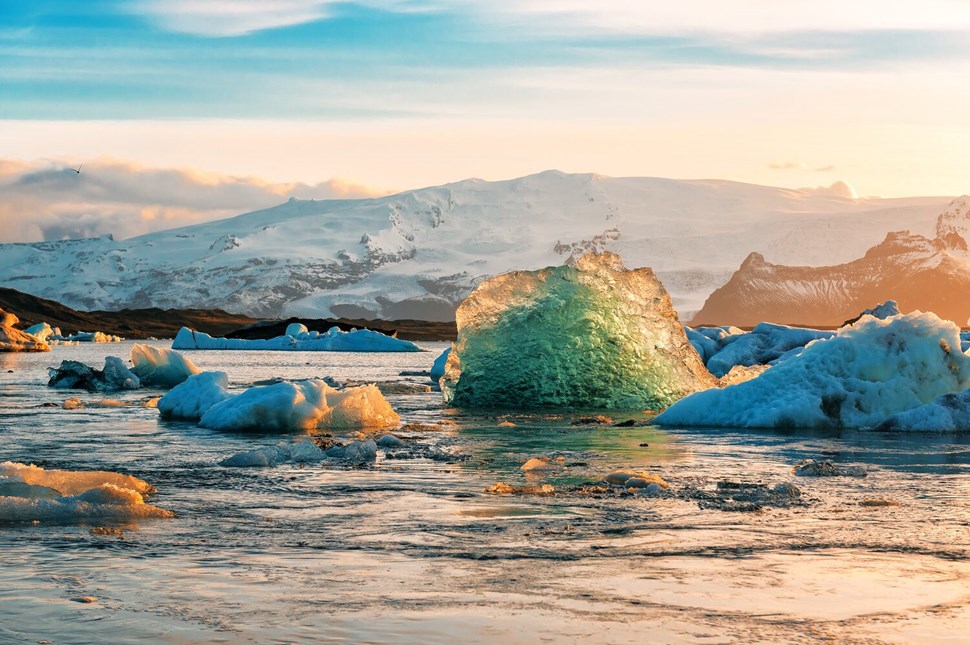 Glacial icebergs bathed in warm glow of sunrise in Icelandic lagoon.