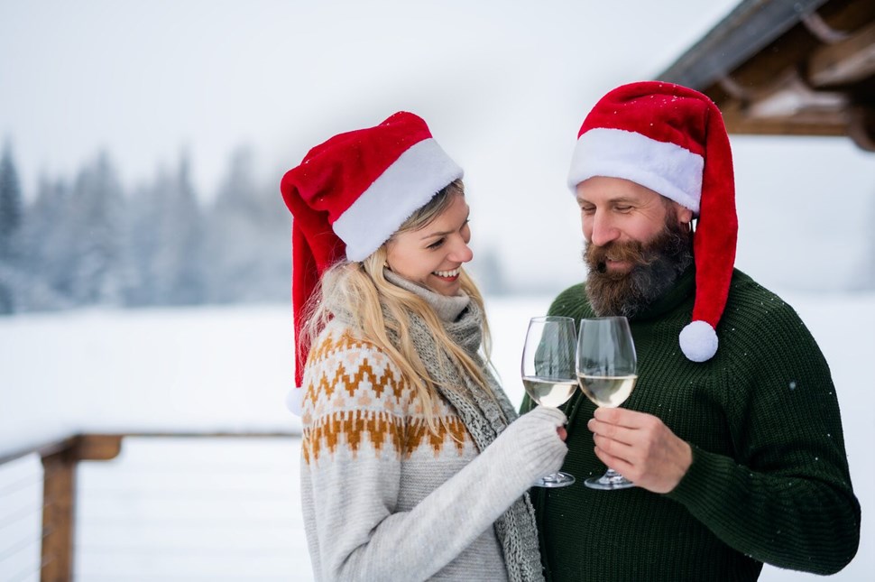 Couple in Santa hats sharing a toast with wine glasses in a snowy landscape.