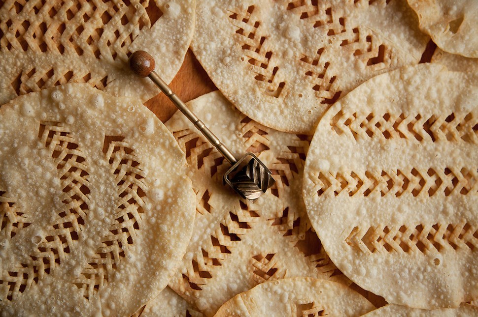 A close-up of traditional Icelandic laufabrauð, intricately patterned flatbreads, with a special cutting tool.