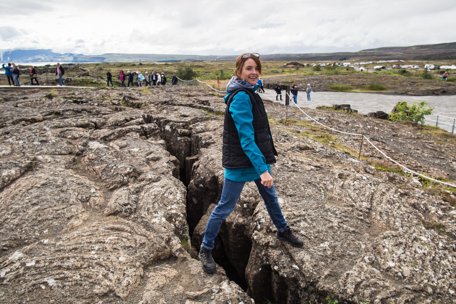 Tourist stepping over fissure in rocky terrain of Icelandic geological site.