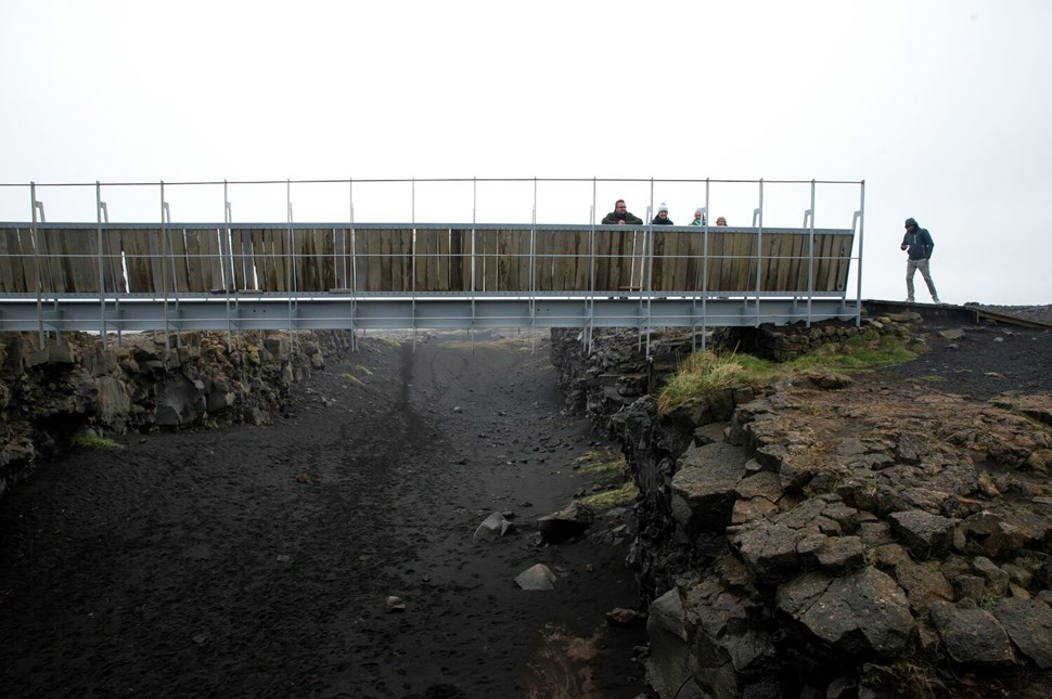 Visitors on bridge over volcanic rift at atmospheric Icelandic tourist site on misty day.