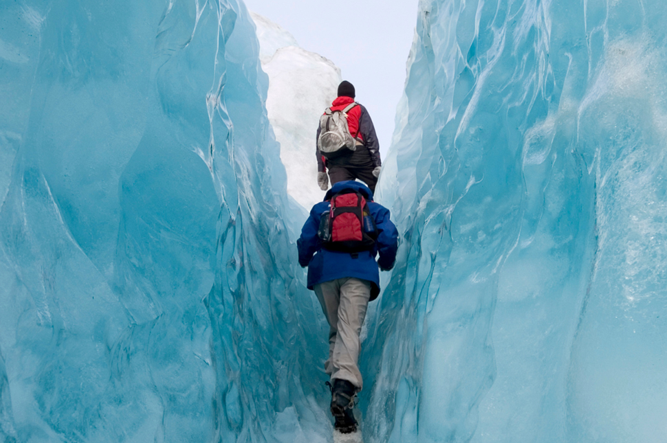 Two people walking through ice walls on a glacier hike