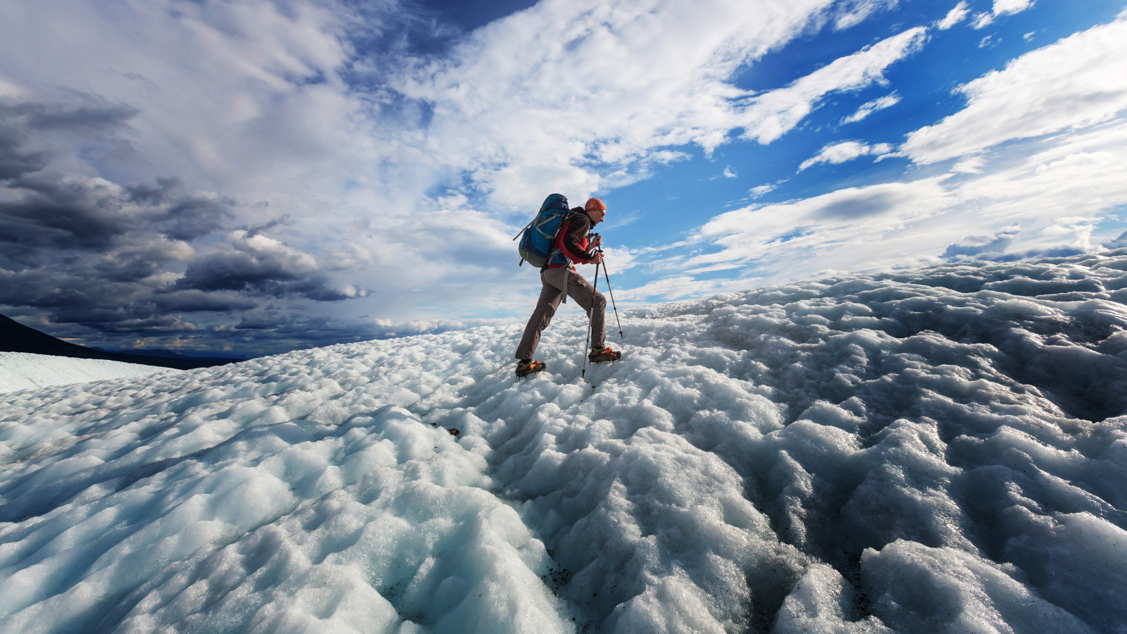 Man walking up a glacier with walking poles and crampons