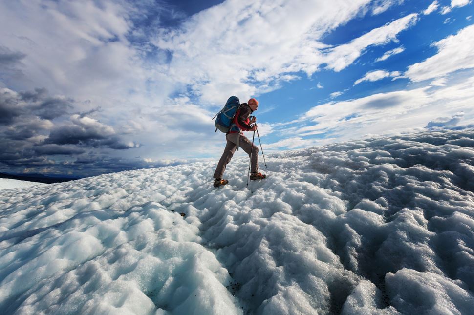 Man walking up a glacier with walking poles and crampons