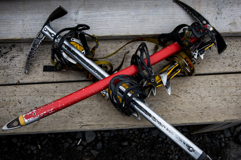 Two ice axes with crampons strapped to them crossed over one another on a wooden step