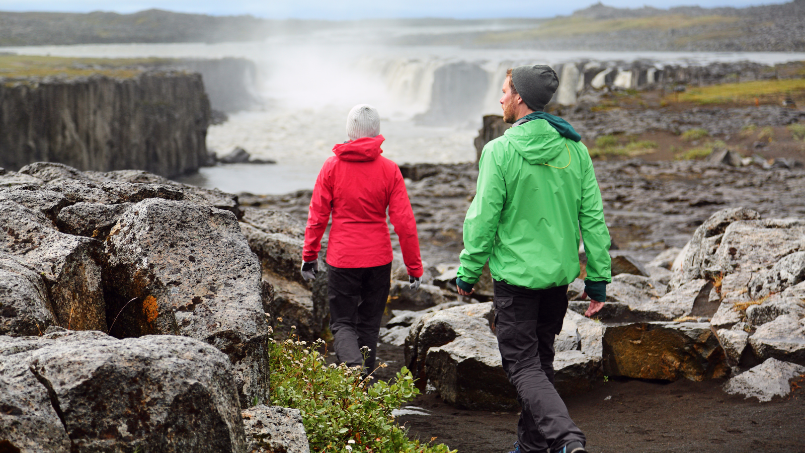 A couple in waterproof coats walking towards Selfoss Waterfall in Iceland