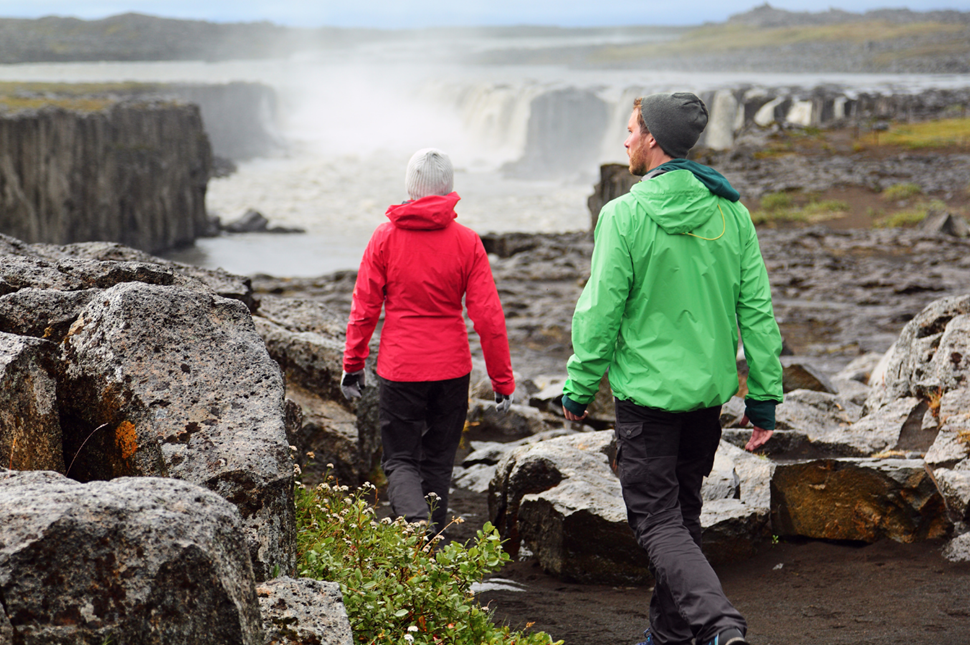 A couple in waterproof coats walking towards Selfoss Waterfall in Iceland