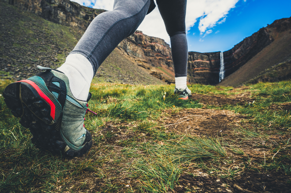 Hiker striding towards the Hengifoss Waterfall in Iceland with blue skies overhead