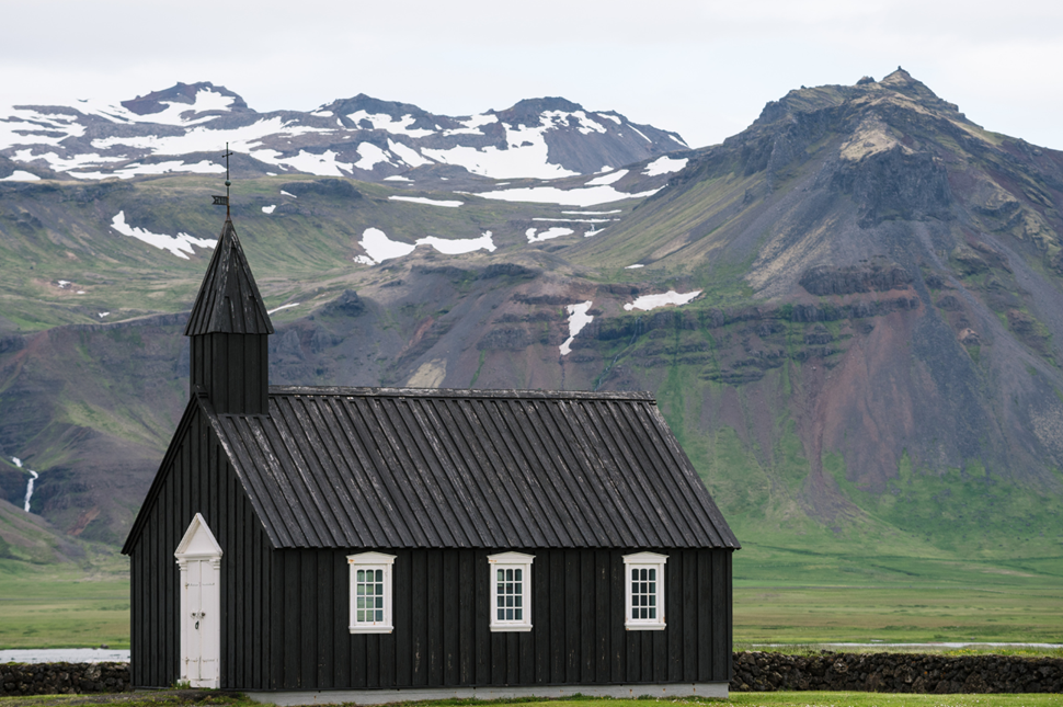 Budir church, a small black church in West Iceland with green fields and rugged mountains in the background