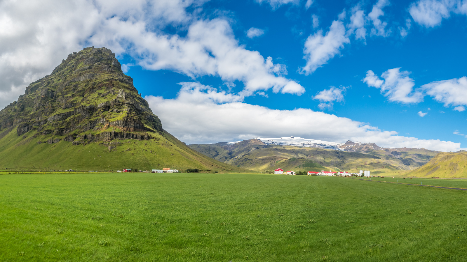 Eyjafjallajökull against a blue sky with green fields in the foreground