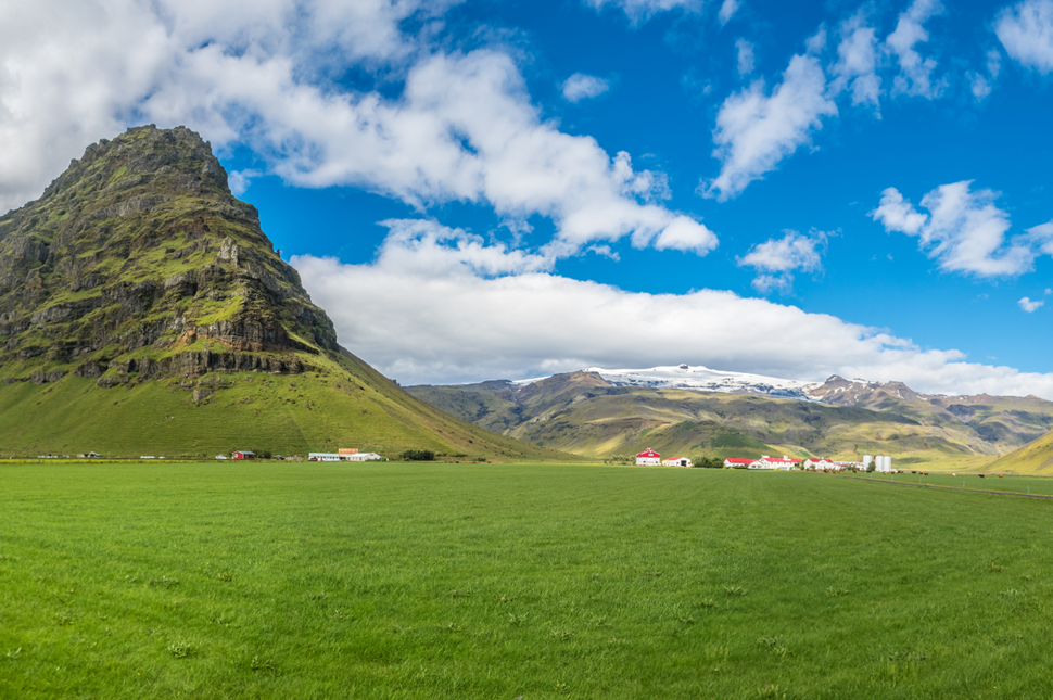 Eyjafjallajökull against a blue sky with green fields in the foreground