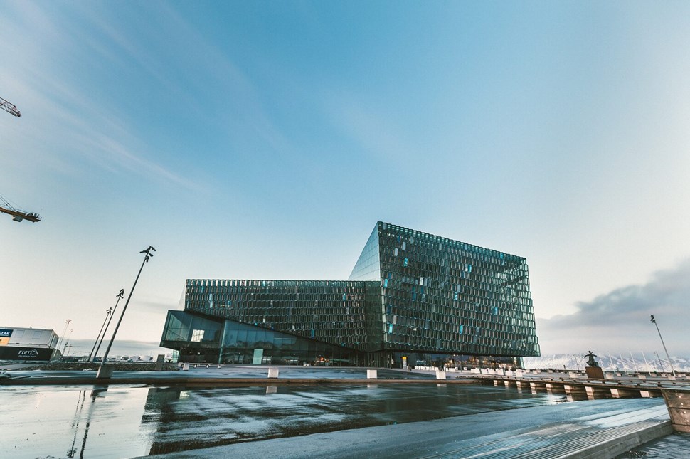 Harpa Concert Hall in Reykjavik stands out with its geometric glass facade reflecting the early morning sky, adjacent to a calm waterfront.